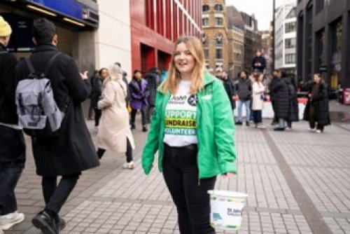St John Ambulance volunteer standing in a busy street carrying a plastic collection bucket.