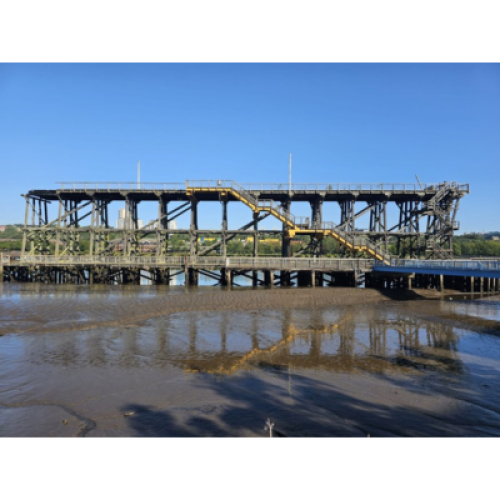 Wooden pier like structure set against blue sky and tidal mud flats