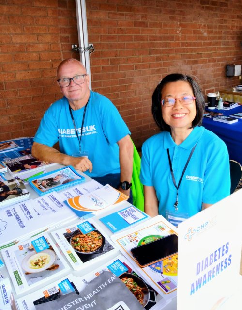 Two volunteers in Diabetes UK blue t shirts hosting an information stand at a community event.