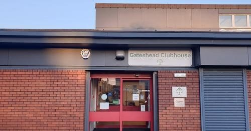 Front of clubhouse with sign.  red brick façade with grey framed glass door.