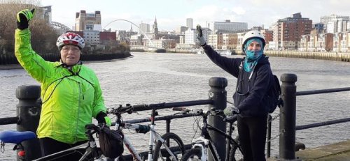 Two riders waving by their bikes on the quayside