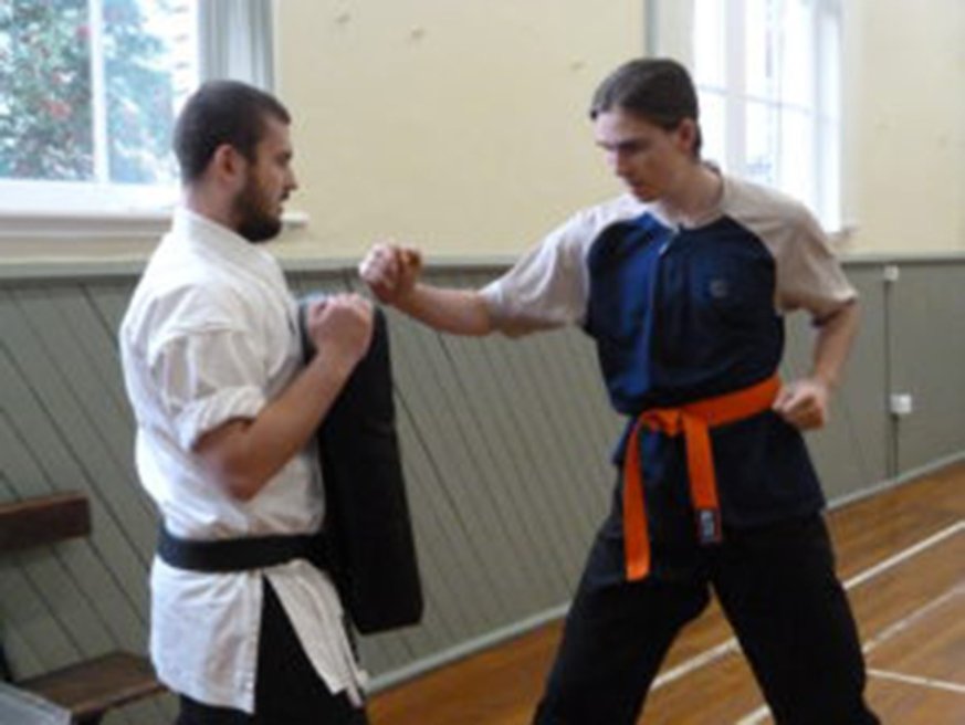 Karate instructor holding punching mat while student practices