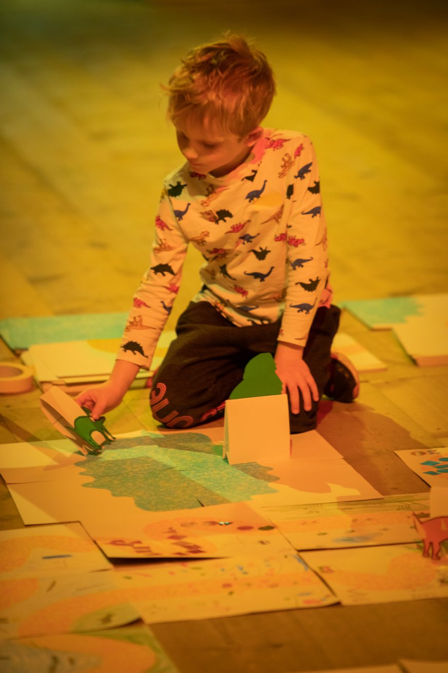 A child makes art on kneeling on the floor surrounded by paper    