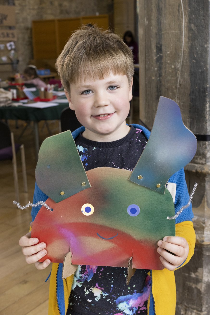 A photo of a boy holding a sculpture he has made. It is made out of various coloured card and materials.
