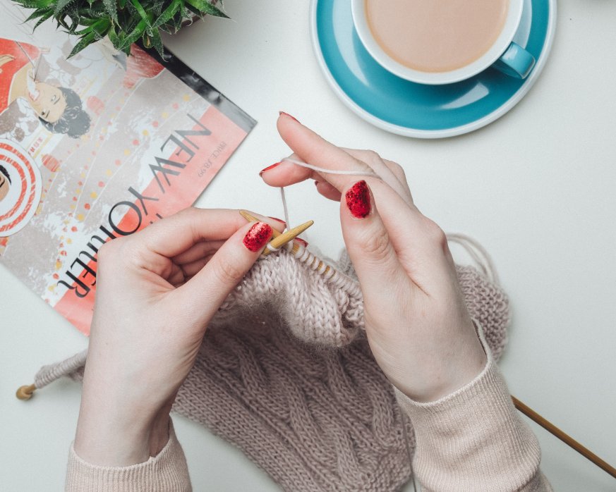 Photo of hands knitting, with a cup of tea by the side