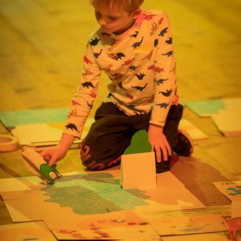 A child makes art on kneeling on the floor surrounded by paper    