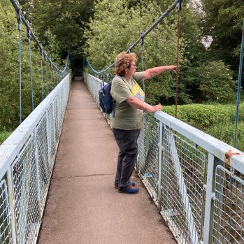 A woman wearing a rucksack points at something on a river while standing on a narrow footbridge.