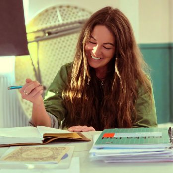 A photo of a woman smiling down whilst writing in a book.