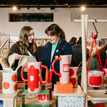 People are browsing a stall filled with ceramics at a makers market