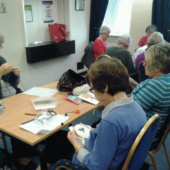Members of the craft group sitting around a table busy working on knitting and embroidery 
