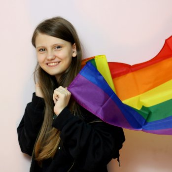 A smiling young person with the Pride flag over thier shoulders