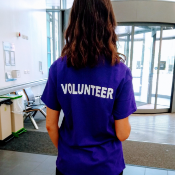 Woman standing back to the camera in a purple top reading VOLUNTEER
