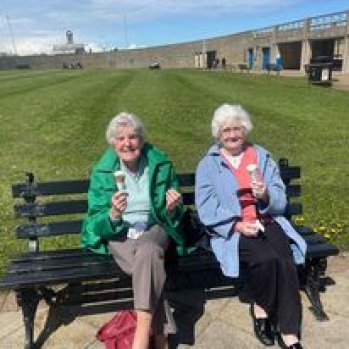 2 women sitting on a bench enjoying an ice cream 